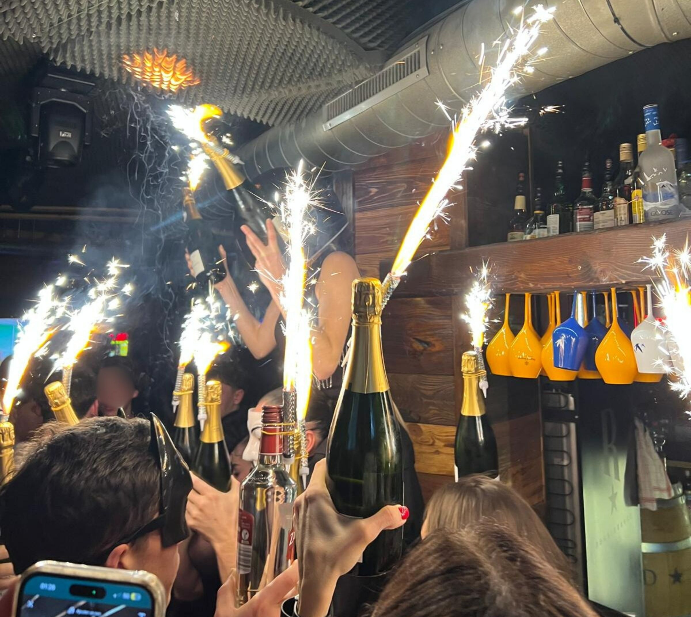 Sparklers attached to champagne bottles held by people in a bar.