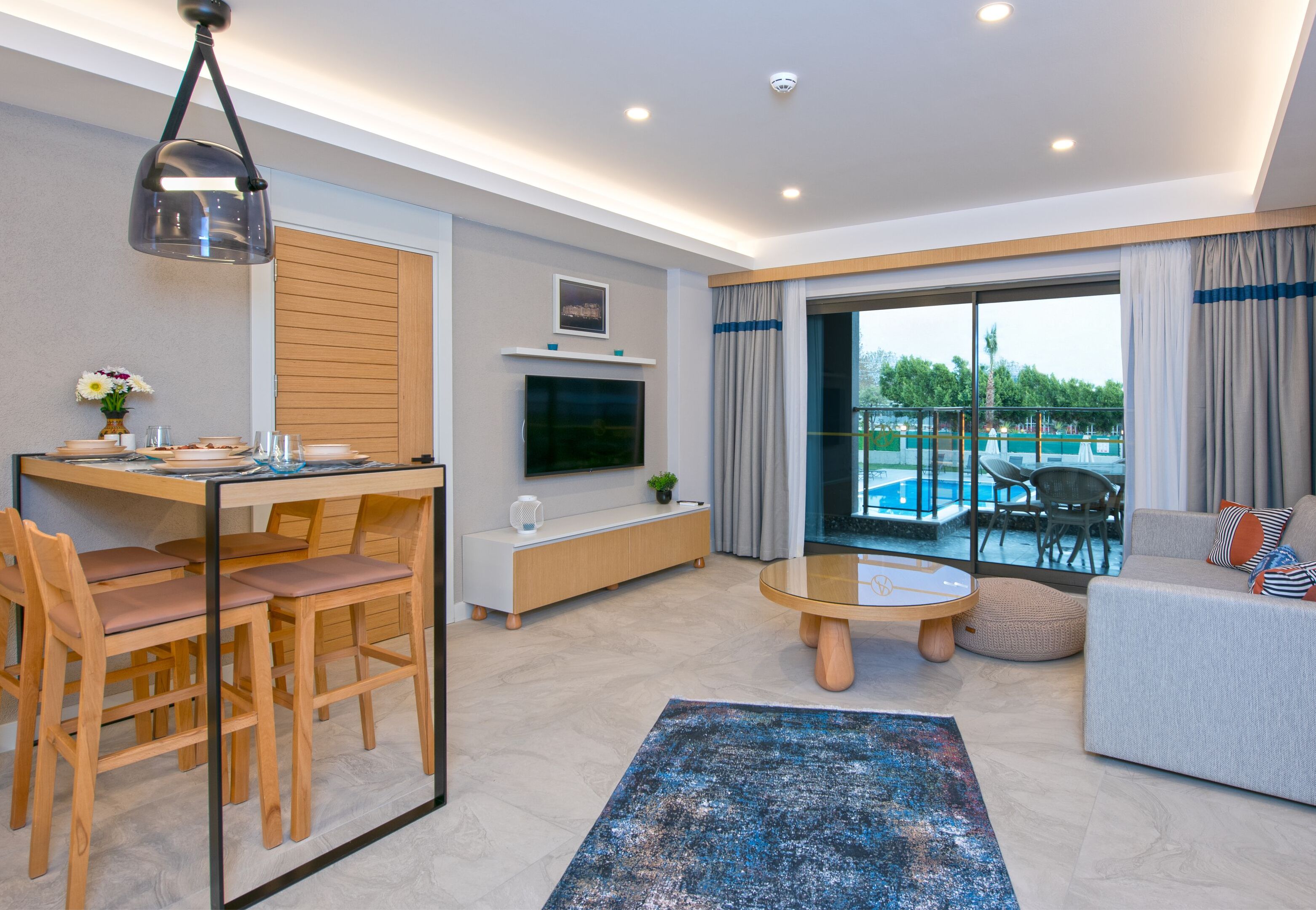 A modern living room with a dining area, a sofa, and a view of an outdoor pool.