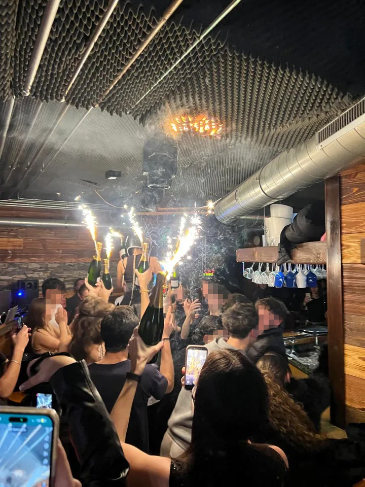 Fire on the ceiling of a bar as people celebrate with champagne bottles that have sparklers.