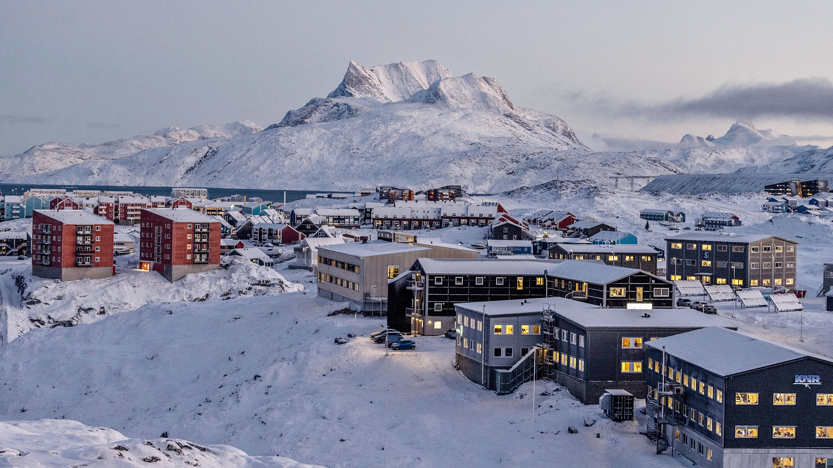 A snowy, mountainous landscape of Nuuk, Greenland, with buildings scattered throughout the foreground and midground.