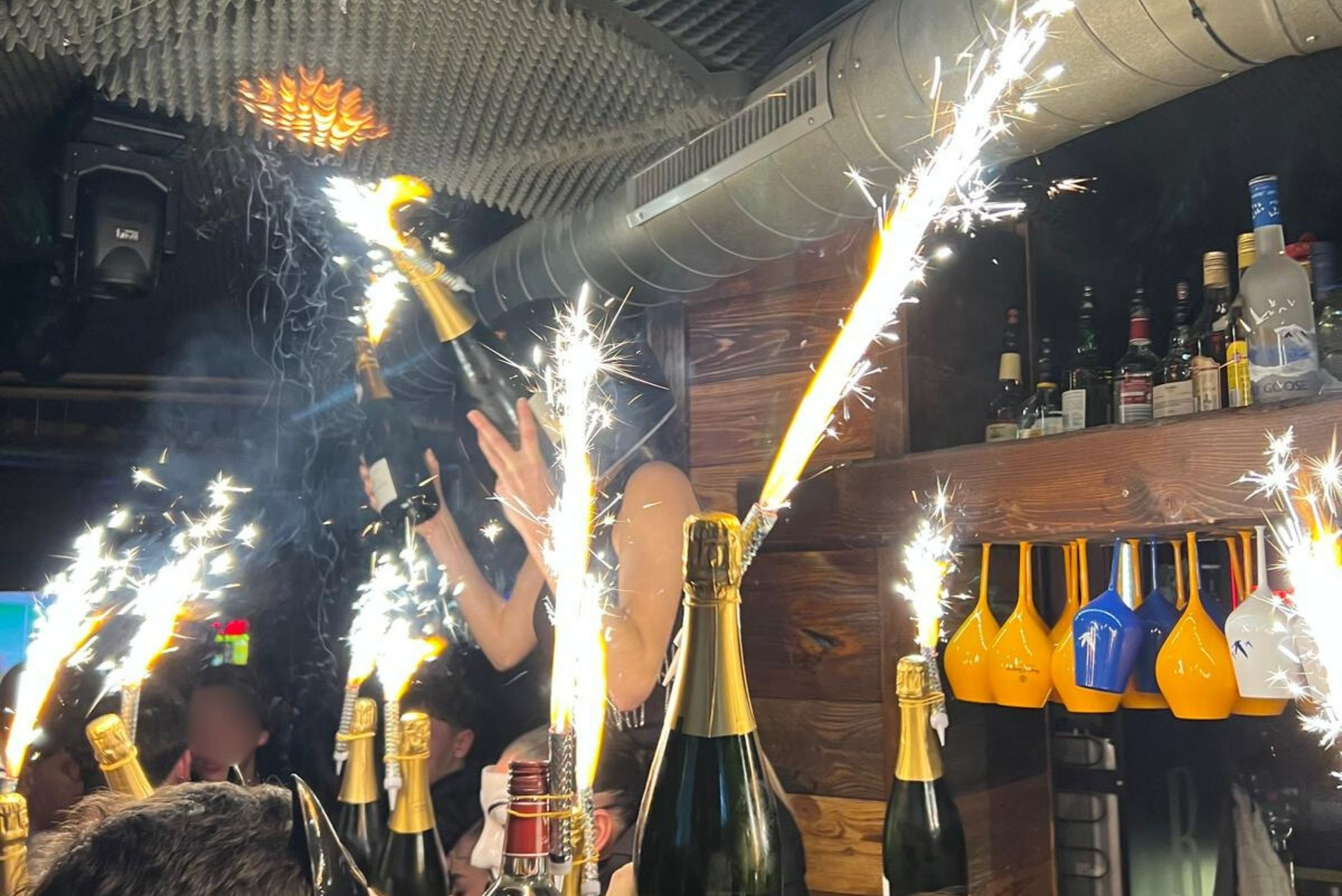 Champagne bottles with sparklers ignite a bar ceiling.