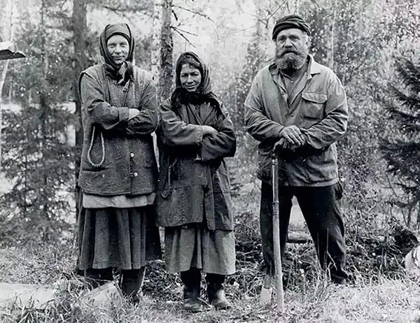 Three people standing outdoors, two women and one bearded man holding a shovel.
