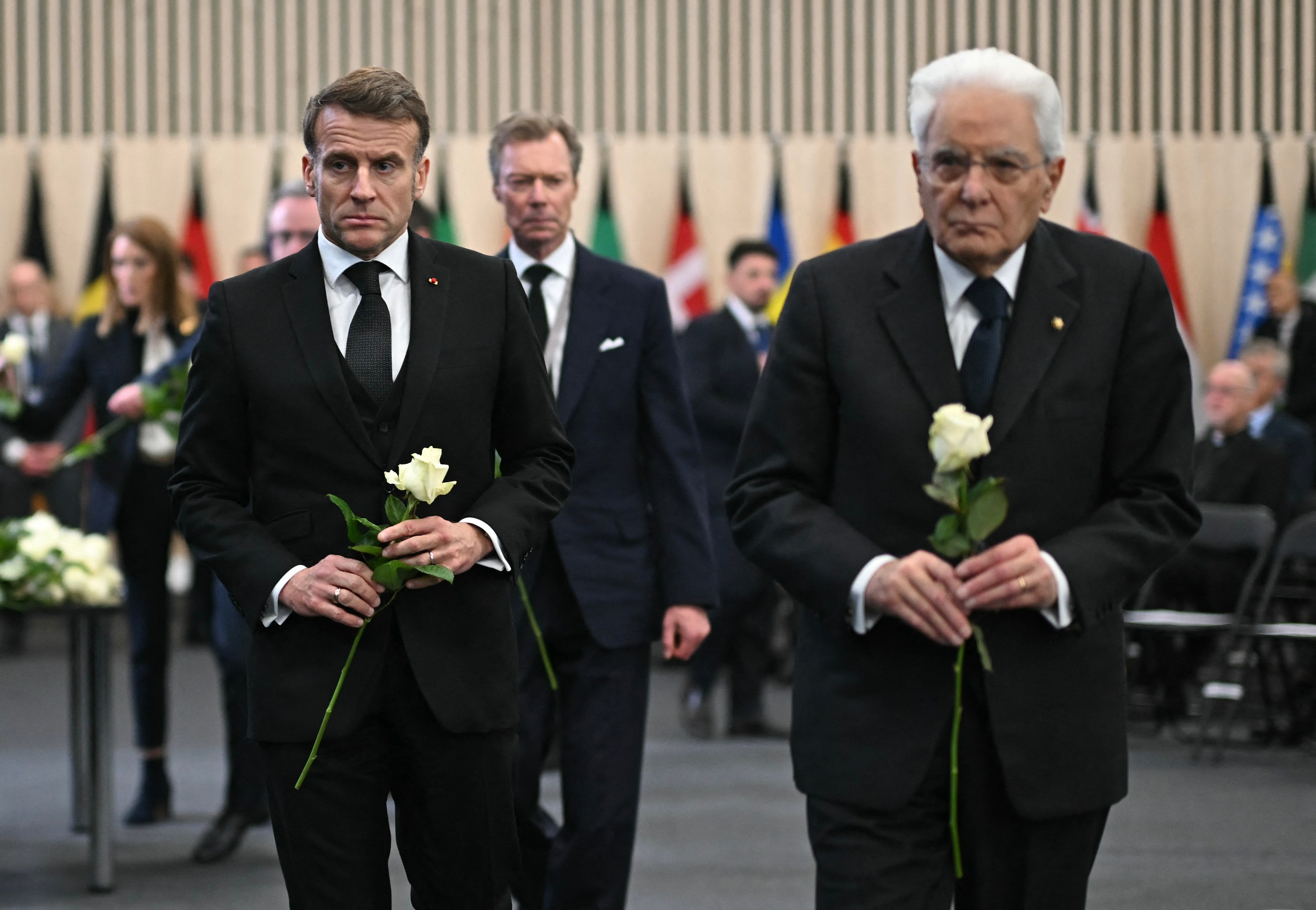 French President Emmanuel Macron and Italian President Sergio Mattarella walk with white roses during a tribute ceremony for victims of a deadly fire.