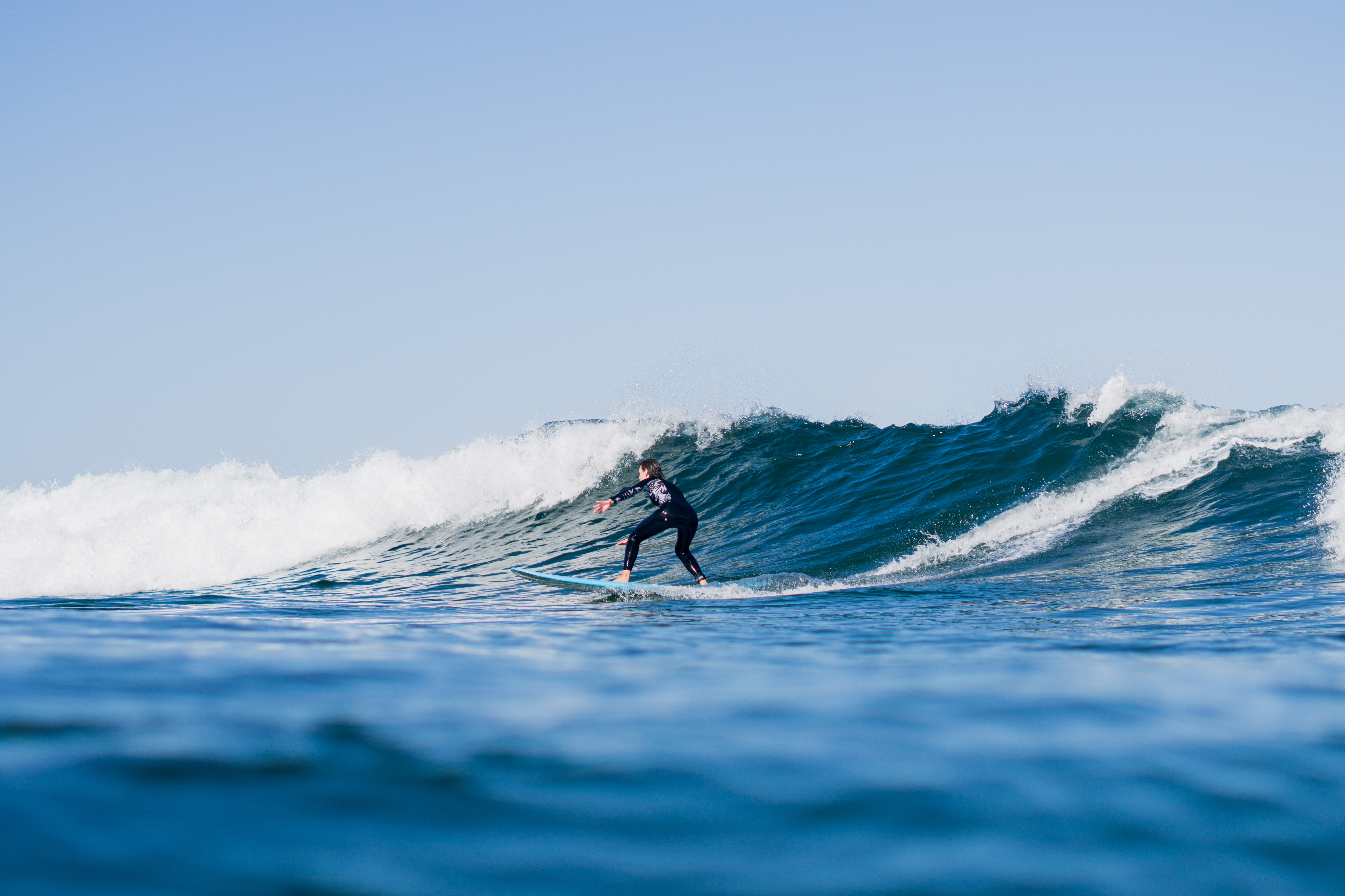 A person in a black wetsuit surfs a wave on a light blue surfboard.
