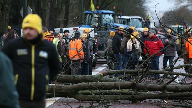 Men gather next to tree trunks placed across a road to block a road