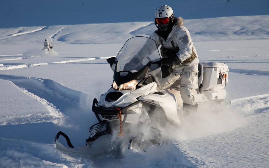 A service member in a snow suit on a snow machine.