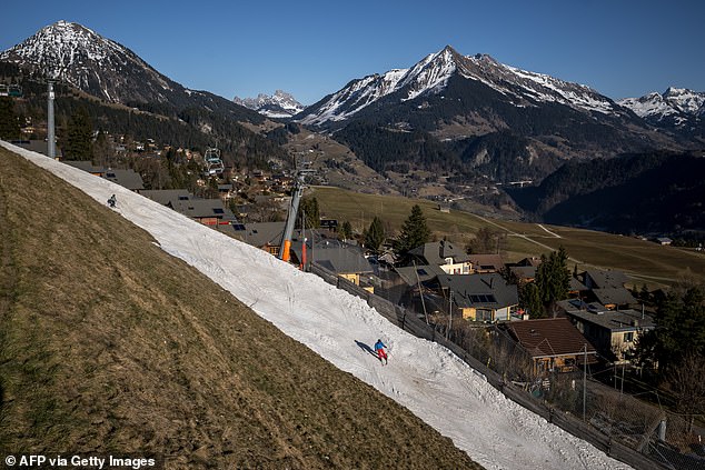 Tourists ski along a poorly snow-covered access slope leading back to the low-altitude resort of Leysin, through a snowless surrounding landscape on December 27, 2025
