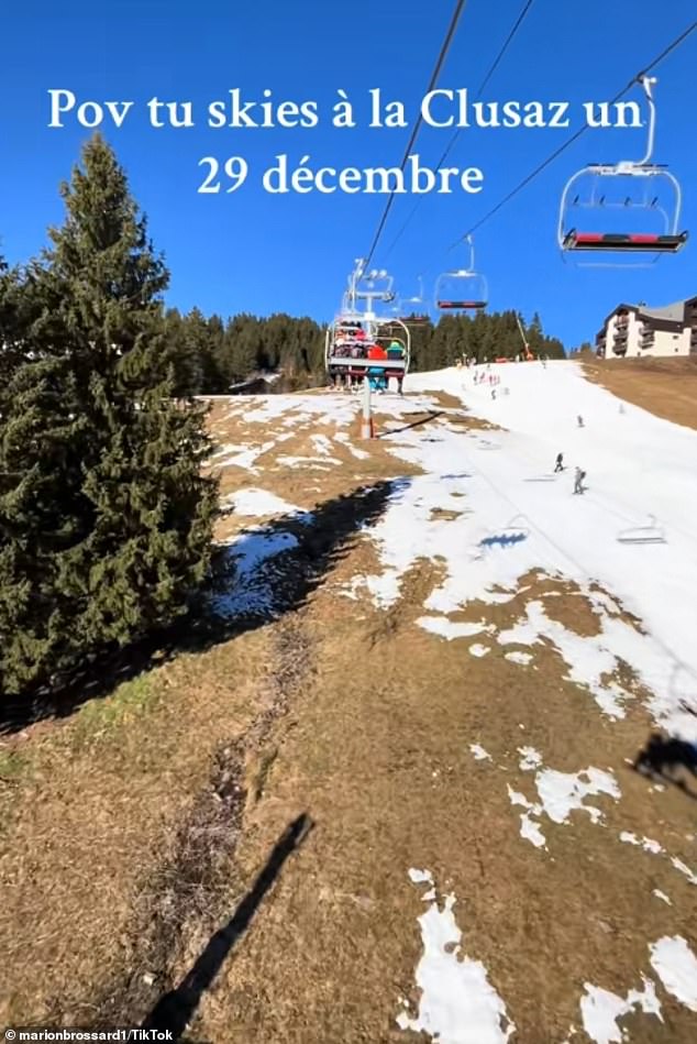 Skiers ride on a ski lift over near naked slopes in La Clusaz, France
