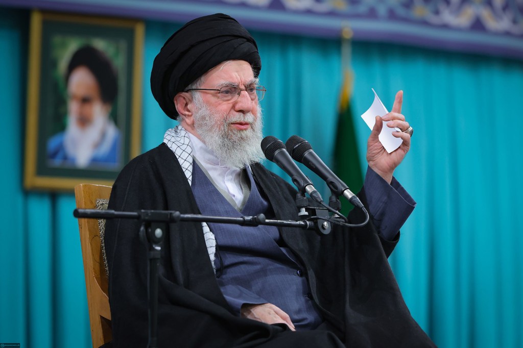 Ayatollah Ali Khamenei speaking at a podium with two microphones.