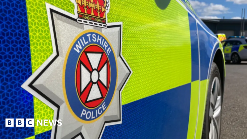 The side of a blue and yellow police vehicle which says 'Wiltshire Police' on the side.