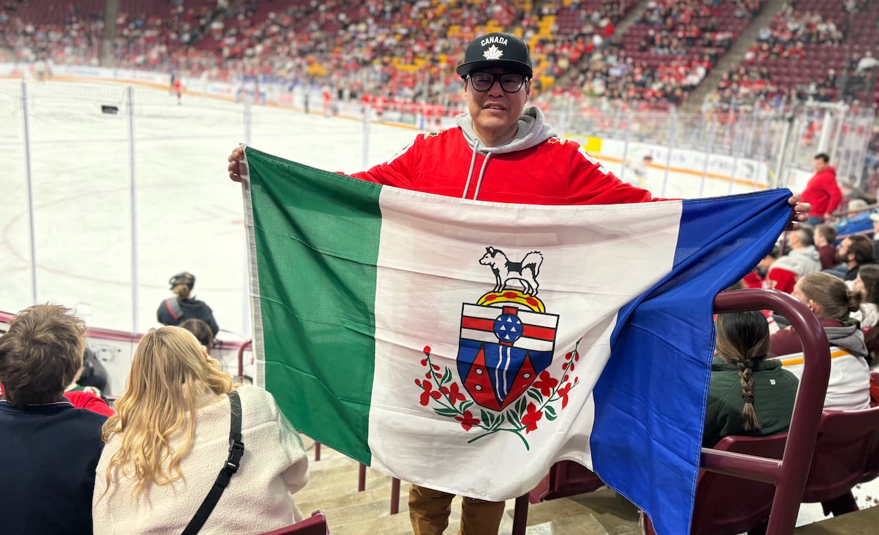 A man stands in the stands at a hockey arena holding up a Yukon flag.