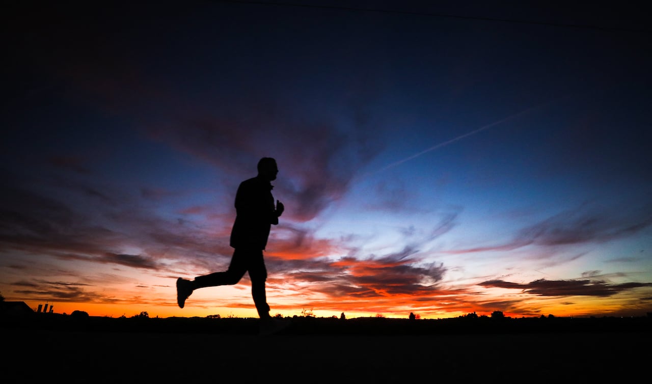 A jogger silhouettes against the evening sky as sun sets.