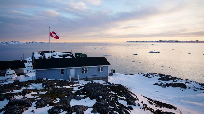 A Greenlandic flag flies above a building overlooking the ocean