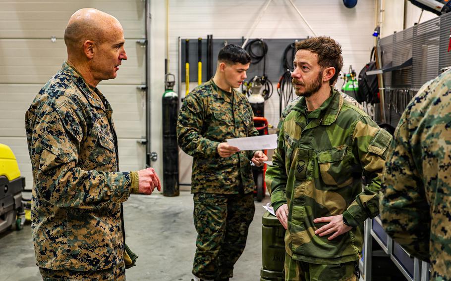 A Marine colonel speaks to a Norwegian service member at a pre-positioning site with troops working in the background.