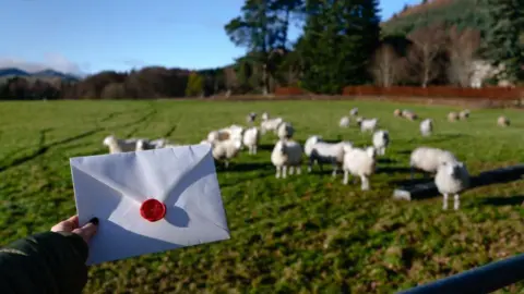 Vienna Tourist Board/Martin Morscher A woman's hand holding a white envelope with a red wax seal. There are sheep and woodlands in the background.