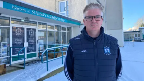 A man with grey hair and a navy St Brigid's body warmer 