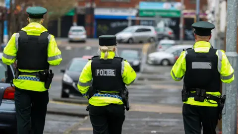PA Media Police officers walking away from the camera, in full hi-vis police gear. 