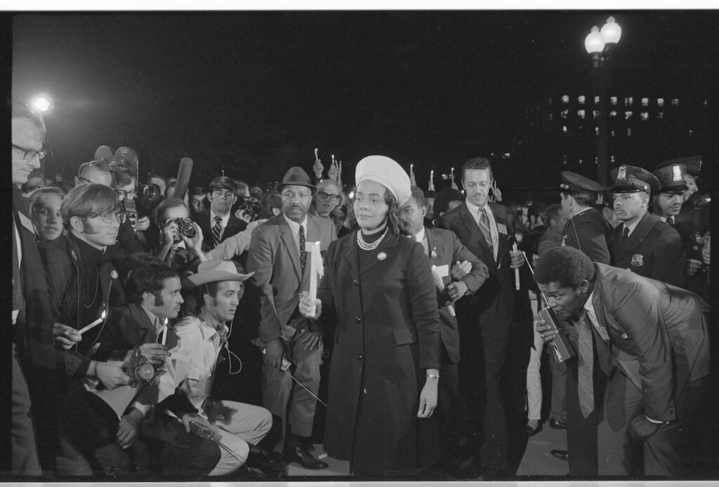 Coretta Scott King’s role in Vietnam anti-war protests Black and white photo of Coretta Scott King holding a candle in her right hand while walking in front of a crowd of people.