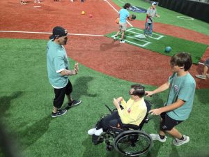 A volunteer pushes a wheelchair user on a field as another participant raises a hand for a high five.