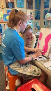 A participant and her mother paint together at a studio table during a Buddy Sports art activity.