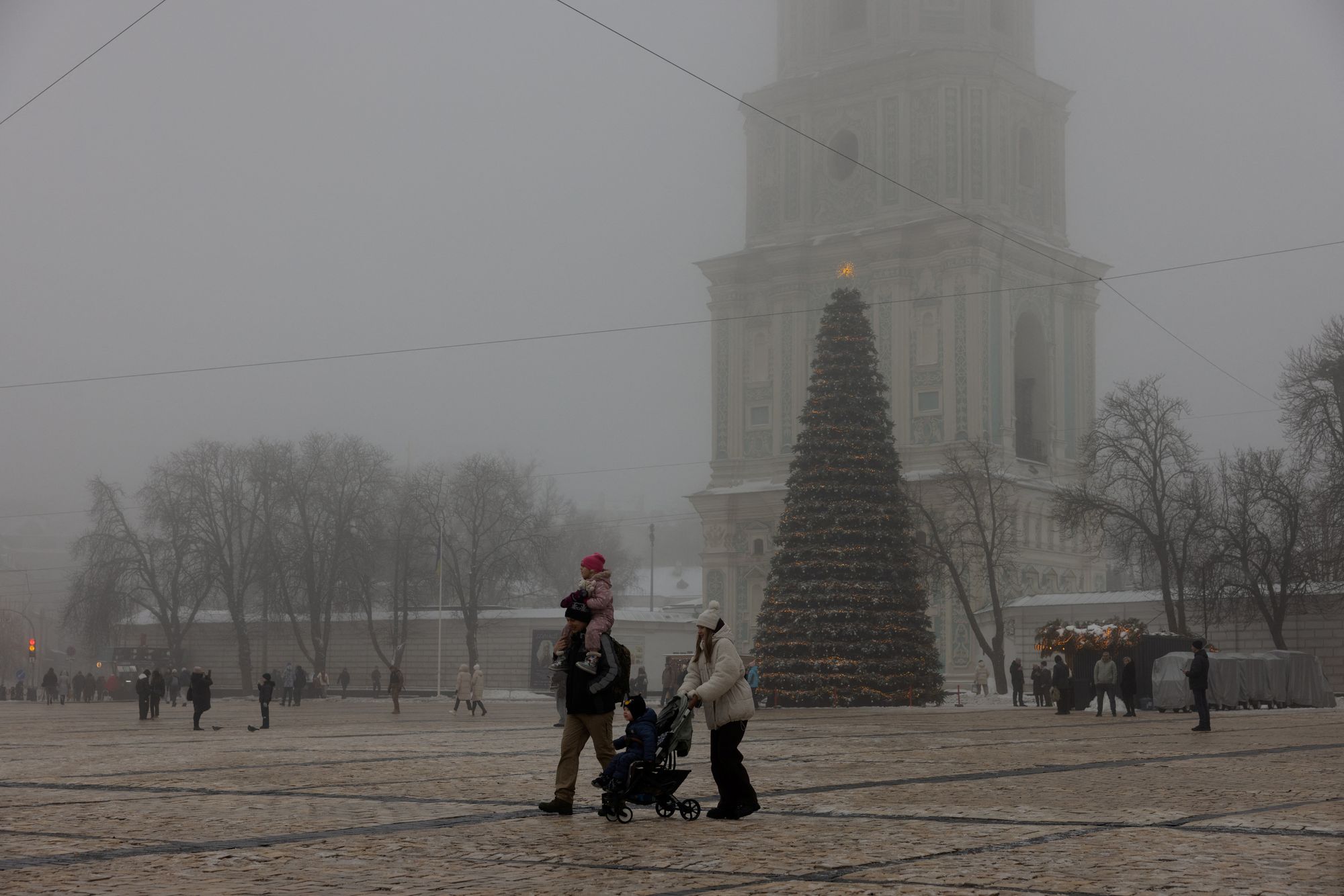 Local residents walk near Kyiv's main Christmas tree on St. Sophia Square on a foggy day in a park in Kyiv