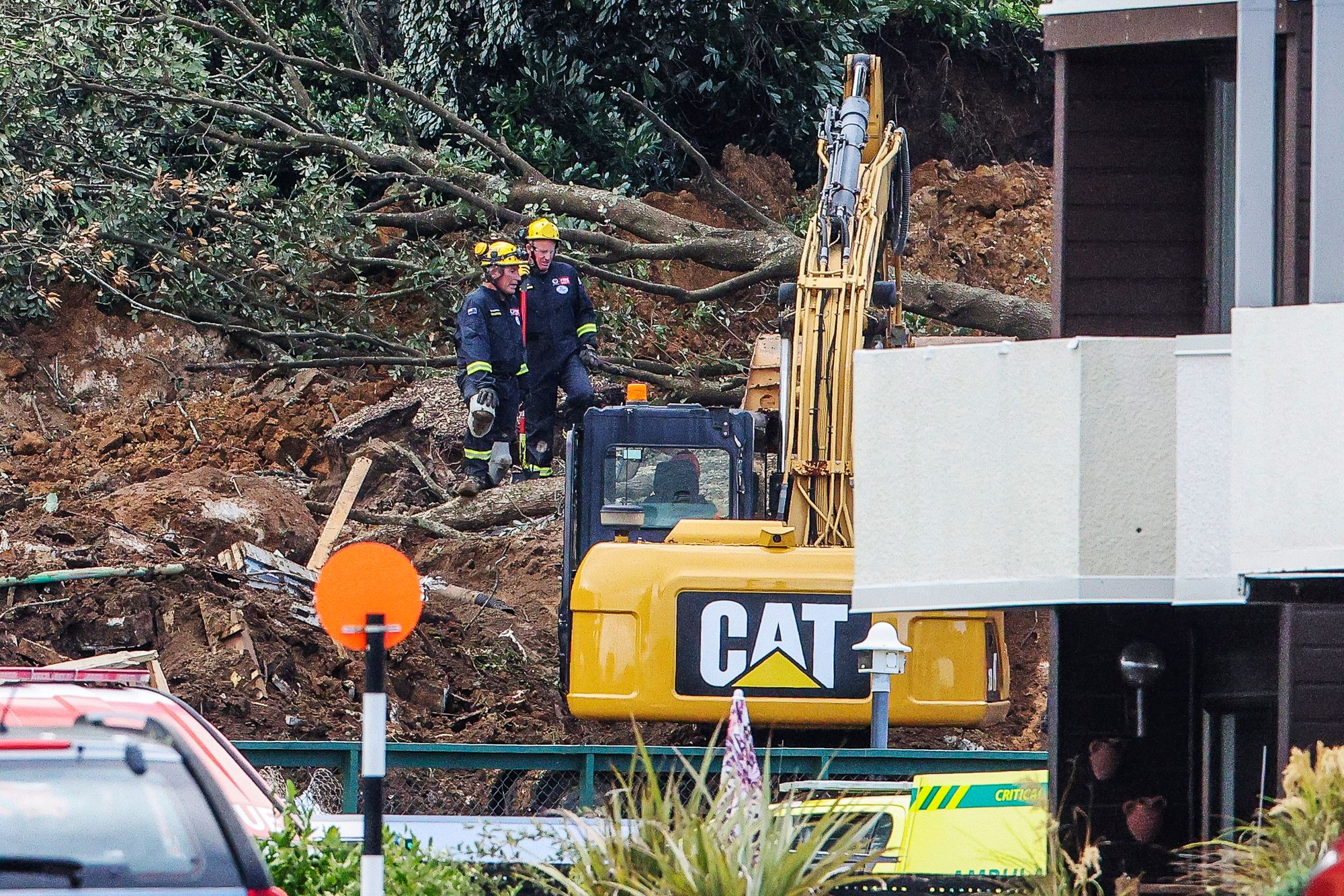 Police and officials stand following a landslide while a search is underway by local emergency services for missing people at Mount Maunganui in Tauranga