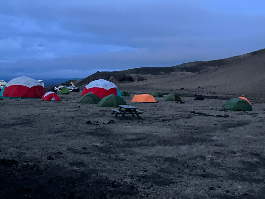 Roughly a dozen tents of various colors and sizes are arranged at a campsite under a dimly lit sky.