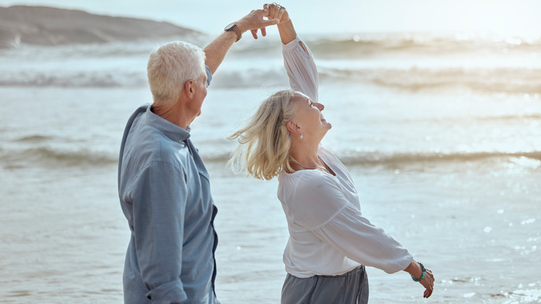 A retired couple dancing happily together on a beach in Greece