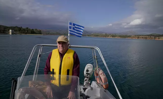 Giorgos Chrysinas, an electricity supervisor for the Water Board (EYDAP), attends the Epiphany ceremony from a small boat at Lake Marathon near Athens, Greece, on Tuesday, Jan. 6, 2026, as receding water levels reflect years of low rainfall. (AP Photo/Thanassis Stavrakis)