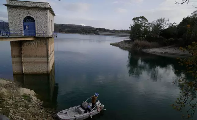 Giorgos Chrysinas Water Board (EYDAP) electricity supervisor adjusts a Greek flag on a small boat at Lake Marathon near Athens, Greece, on Tuesday, Jan. 6, 2026, as receding water levels reflect years of low rainfall. (AP Photo/Thanassis Stavrakis)