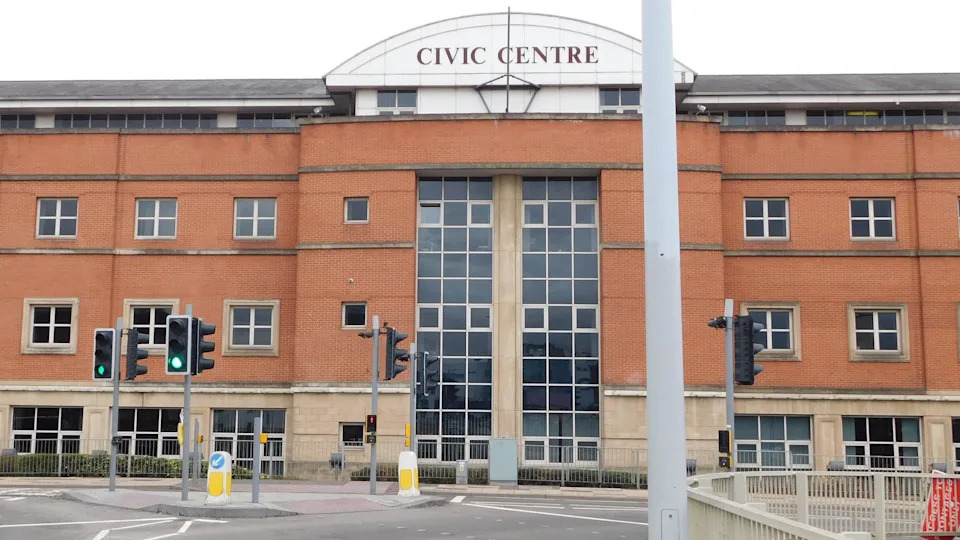 A large orange and cream coloured brick building with a "Civic Centre" sign over the top. It is viewed from the road, next to a traffic light-controlled junction.