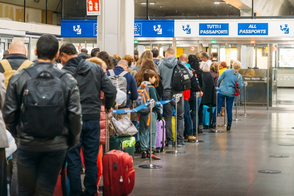 Crowd of travelers lining up with luggage at an airport passport control area.