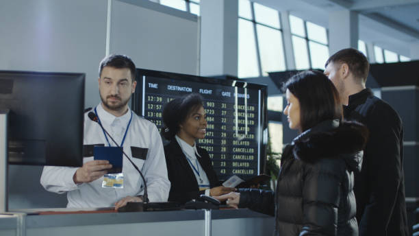 Passengers speaking with airline staff at an airport check-in counter, with a flight information board in the background.