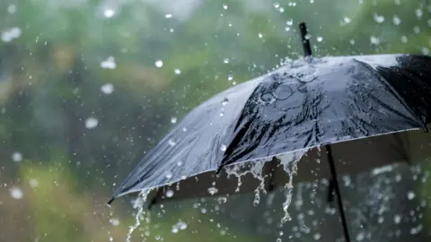 Getty Images A black umbrella is covered with falling water that looks like rain. The background is blurred. 