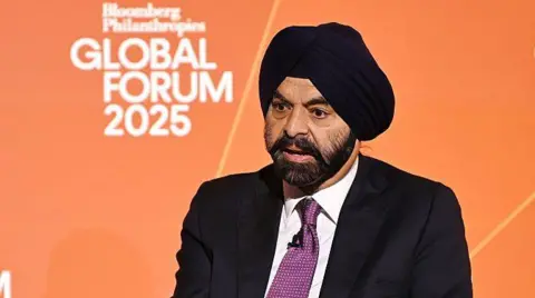 Getty Images An image of Ajay Banga speaking in front of an orange backdrop, while dressed in a black turban and black suit with a purple tie.