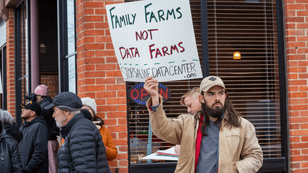 A person with long brown hair and a cropped brown beard holds a sign that says "family farms not data farms."
