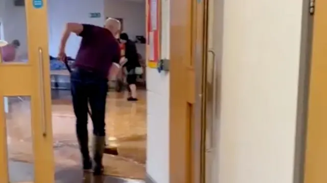 People inside a community centre brushing the ground that is covered with water.