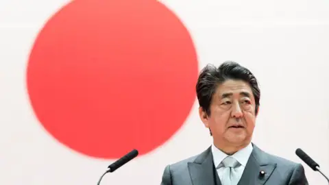 Getty Images Japan's Prime Minister Shinzo Abe speaks during the graduation ceremony of the National Defense Academy on March 22, 2020. The flag of Japan is in the background