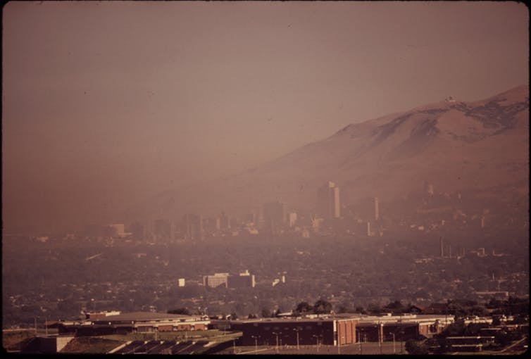 A curtain of smog obstructs the view of a city and the mountains behind it.