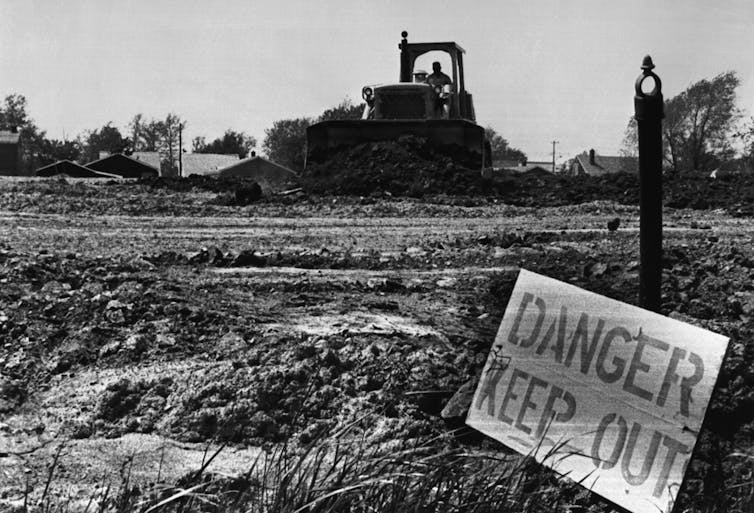 A bulldozer pushes dirt across open land, marked with a sign saying 'Danger, keep out.'