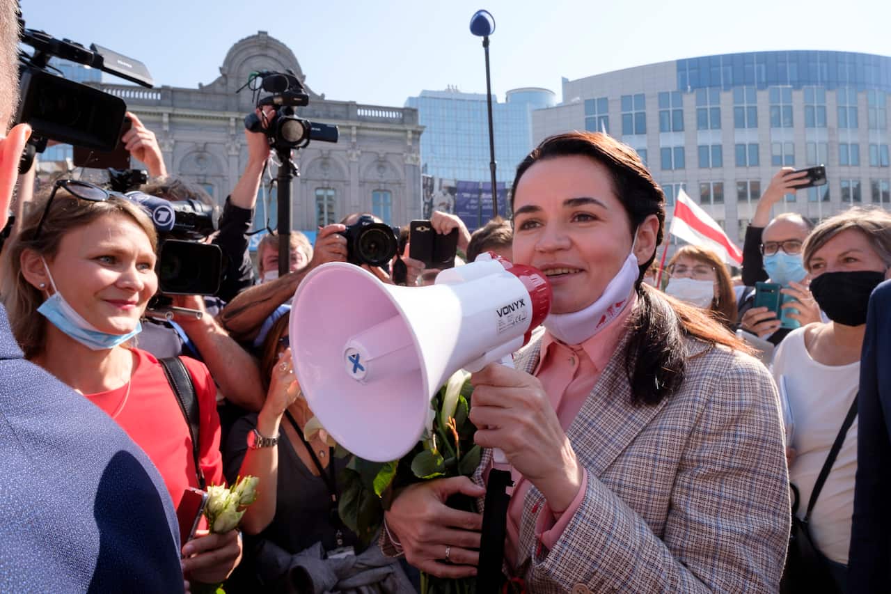 A woman speaks into a white-and-pink megaphone, surrounded by a crowd of supporters and members of the press.