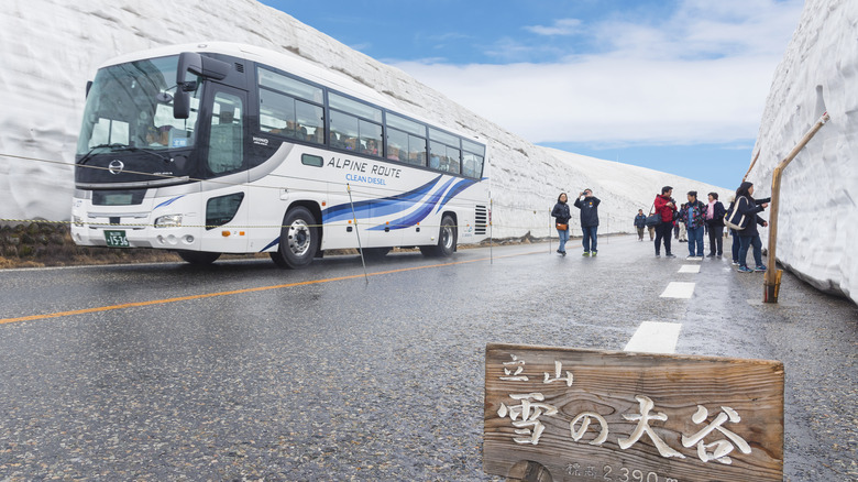 Tourists on the road in the Tateyama Snow Corridor with a bus sitting behind them