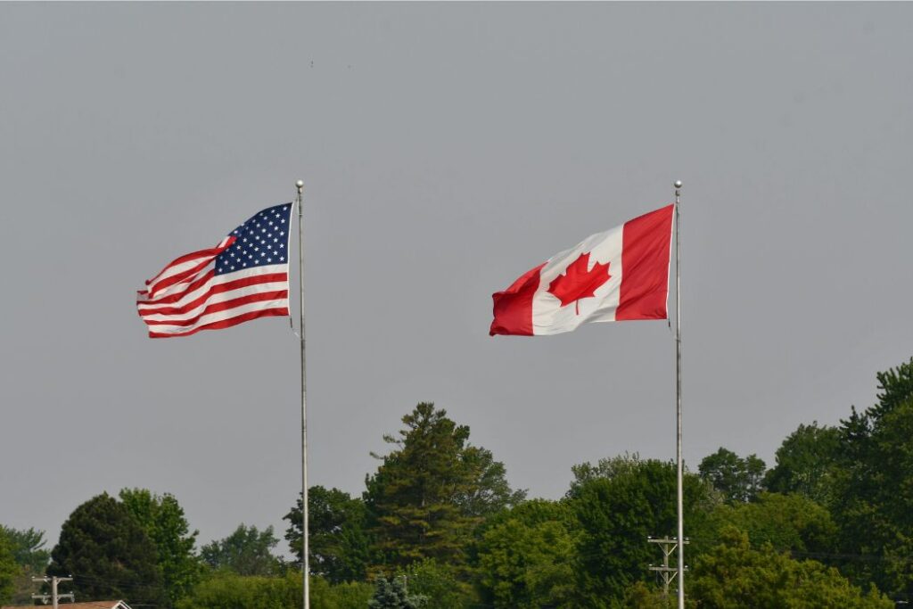 Canada America US flag | BetaKit A Canadian and American flag flap int eh wind, side by side.
