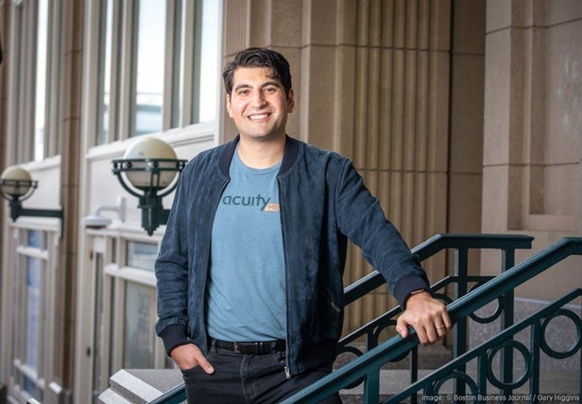 Mike Monovoukas wears an AcuityMD shirt and a dark jacket while standing on stairs outside a building.