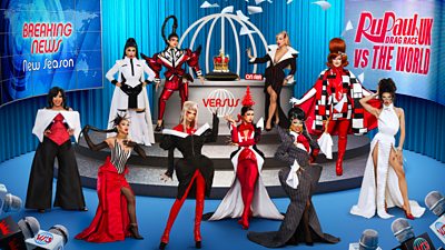 Ten drag queens stand in a fake news studio with "breaking news: new season" flashing up on a screen. The other screen says "RuPaul's Drag Race UK vs The World." The queens are all dressed in black, white and red ensembles, posing around an opulent crown in a cage. 
