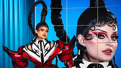 A drag queen (Fontana) poses in a larger-than-life red and black zebra striped outfit with a huge protruding ponytail