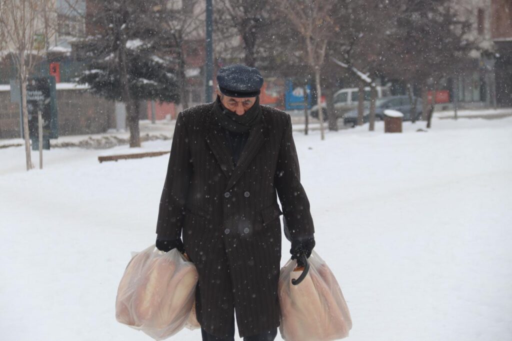 A resident struggles to carry grocery bags through falling snow as snowfall resumes in Kars, Türkiye, Jan. 23, 2026. (AA Photo)