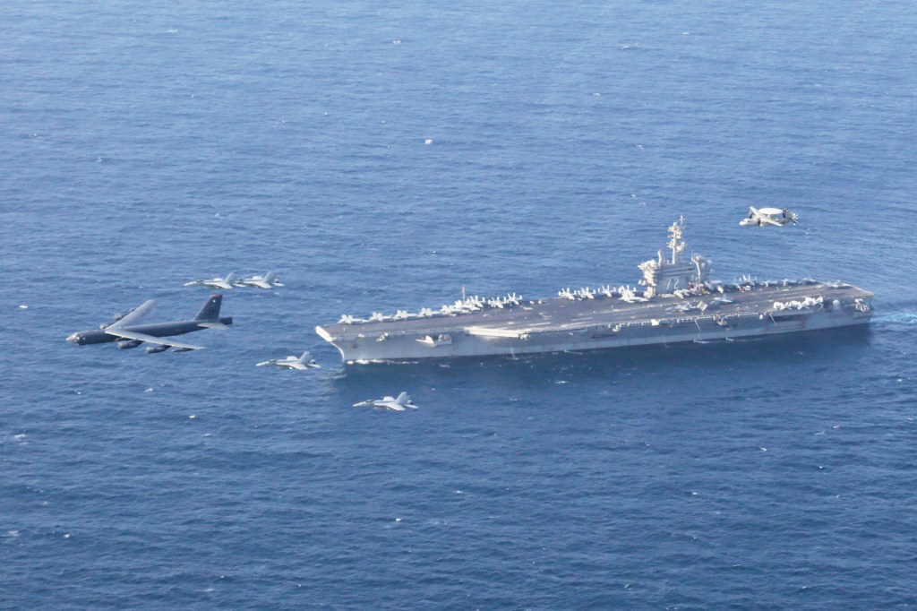 Aerial view of the USS Abraham Lincoln carrier, accompanied by a B-52H Stratofortress bomber and several fighter jets, performing joint exercises in the Arabian Sea.