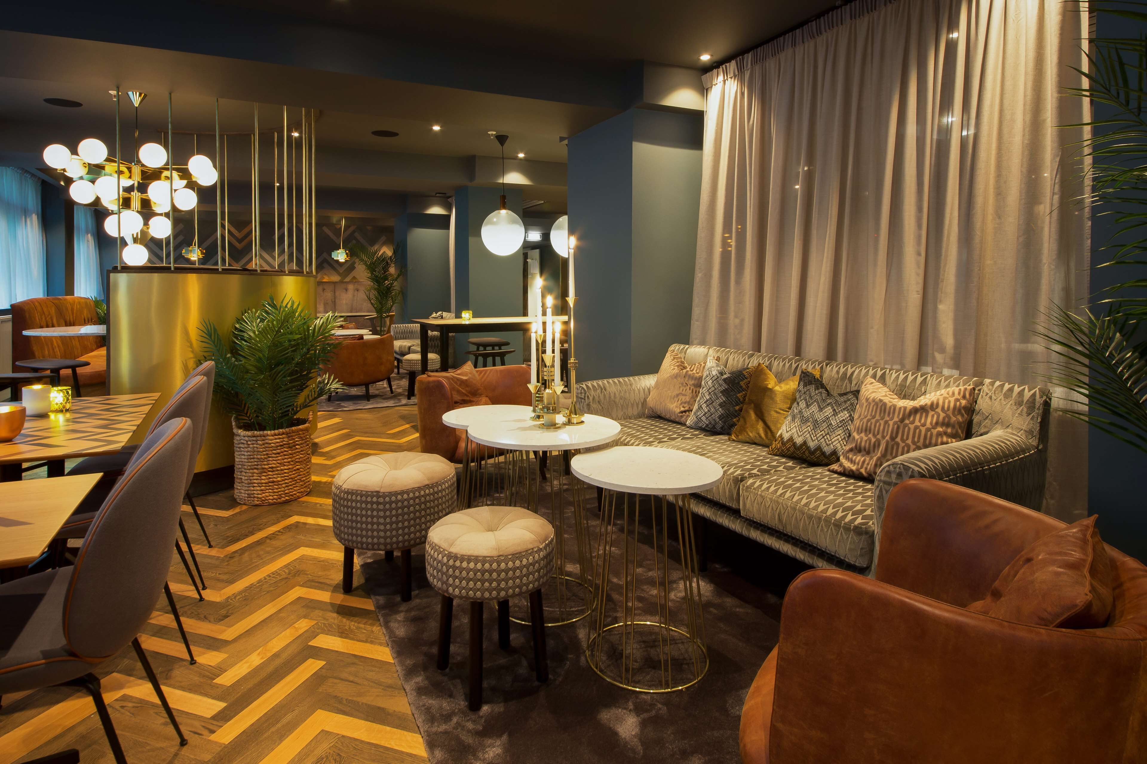 Lounge area with a patterned sofa, brown leather armchairs, round tables, and a wooden floor with a chevron pattern.