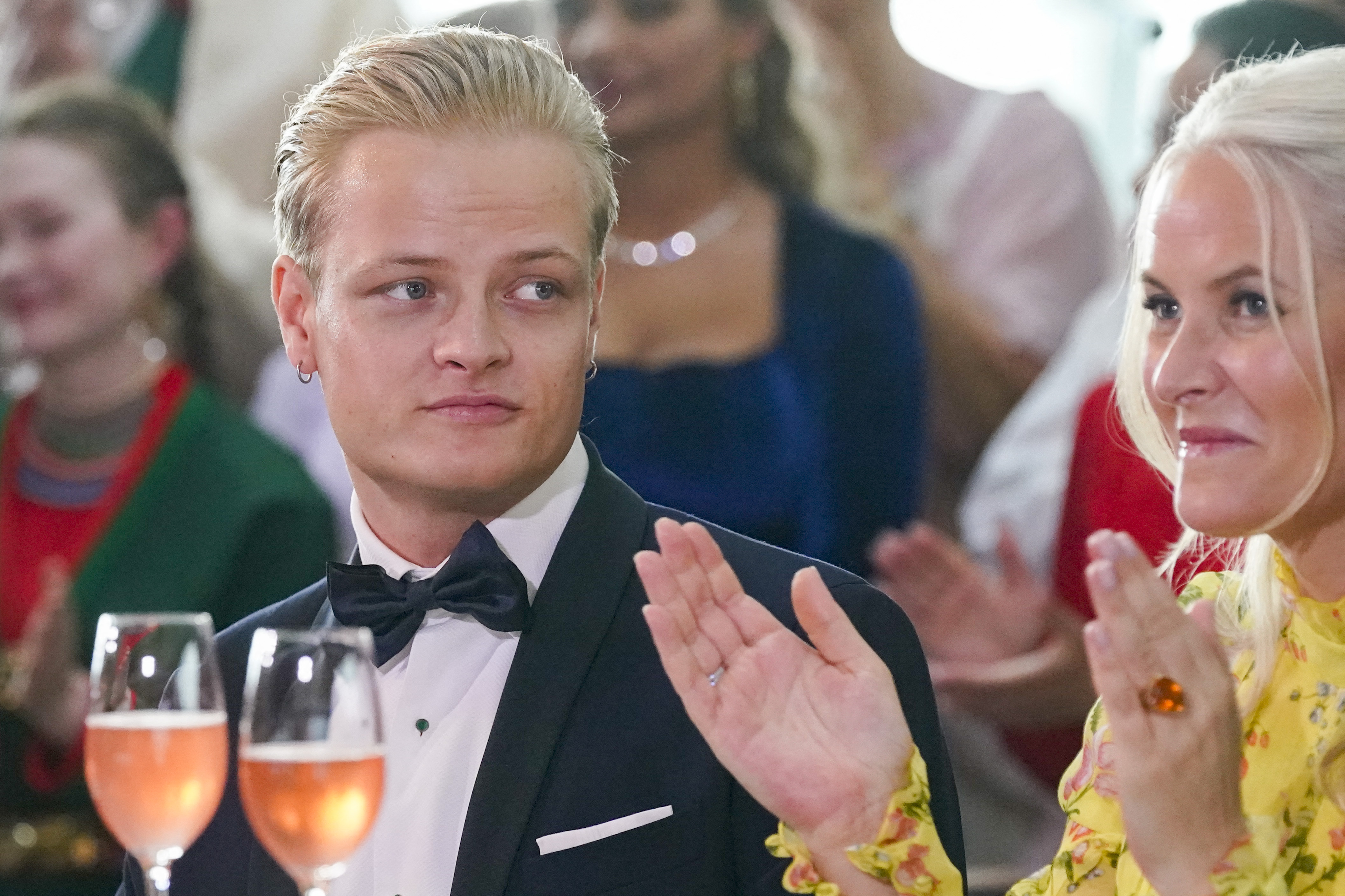 Marius Borg Høiby in a tuxedo looking left next to Crown Princess Mette-Marit of Norway, who is clapping.
